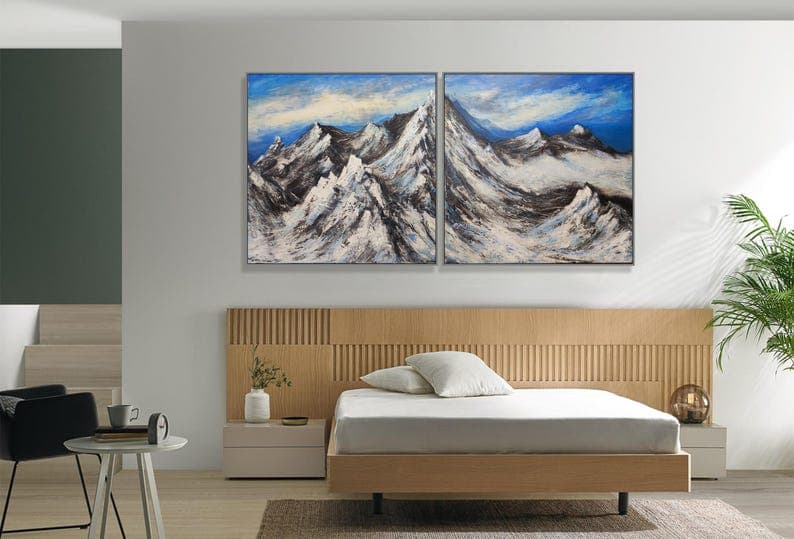 Two textured mountain paintings arranged above a light wood bed.